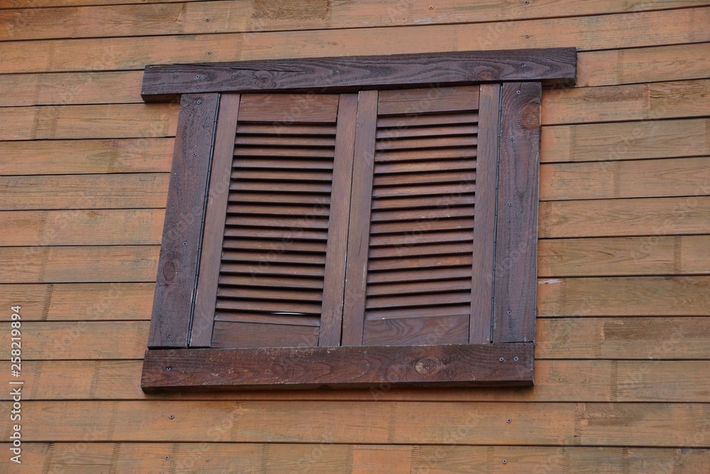 window covered with brown wooden shutters on the wall of boards