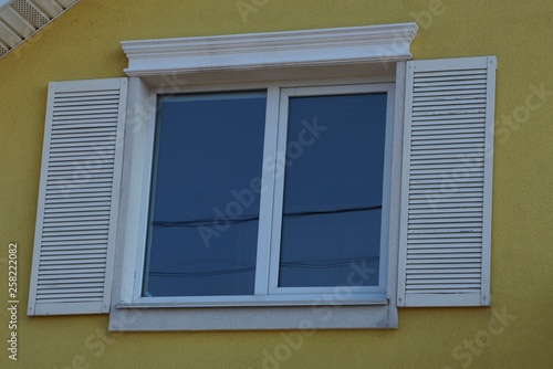 white window with open wooden shutters on the yellow wall of the building