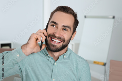 Young man laughing while talking on phone in office