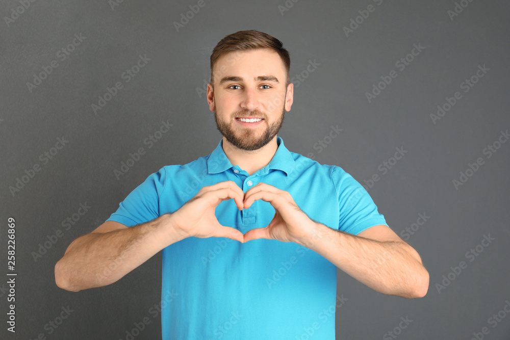 Young man making heart with his hands on grey background Young man making heart with his hands on grey background
