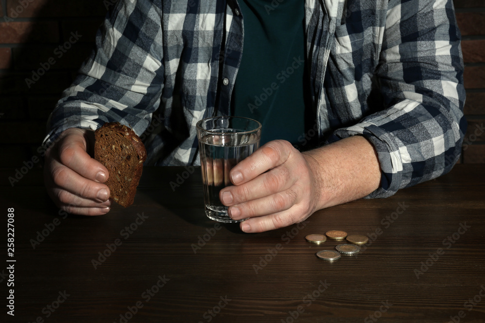 Poor senior man with bread and glass of water at table, closeup