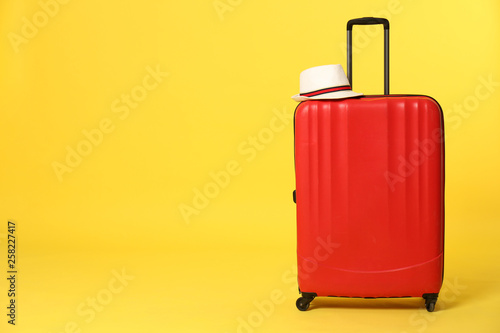 Bright suitcase with hat on color background. Space for text