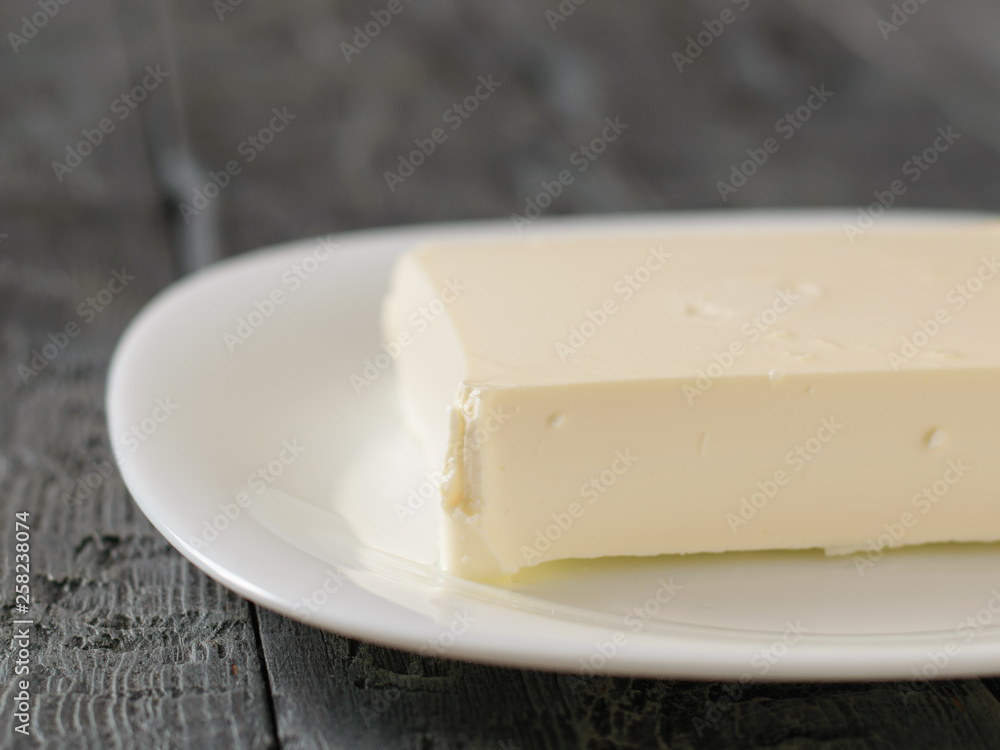 A large piece of cheese on a white plate on a black table. The view from the top. Dairy product.