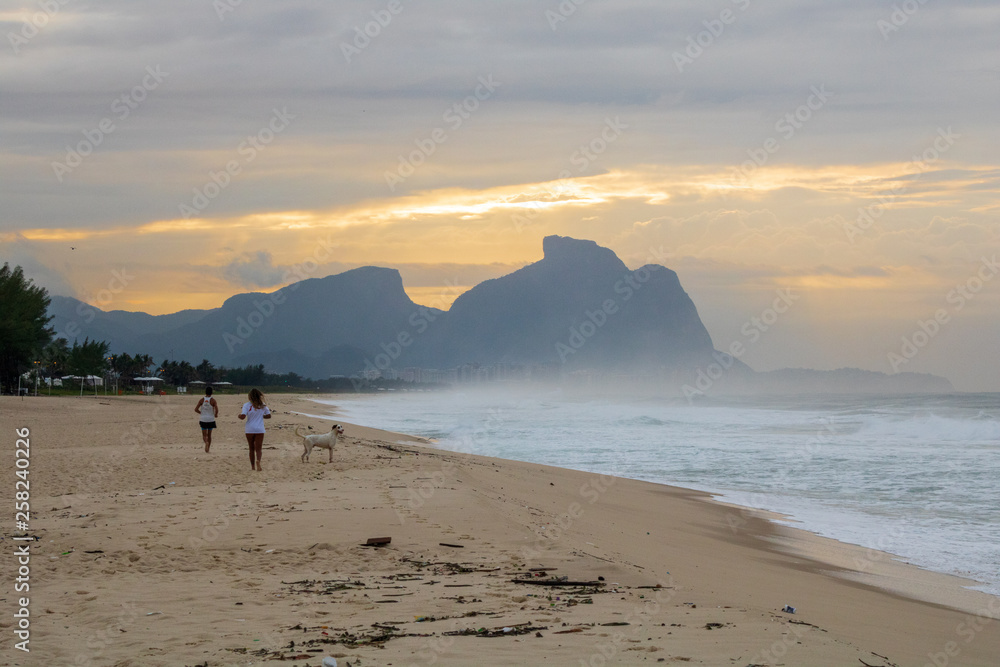 couple and dog running on the beach of Barra da Tijuca in a beautiful dawn with the stone of Gavea in the background - Rio de Janeiro Brazil couple and dog running on the beach of Barra da Tijuca in a beautiful dawn with the stone of Gavea in the background - Rio de Janeiro Brazil
