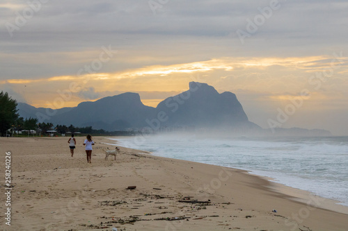 couple and dog running on the beach of Barra da Tijuca in a beautiful dawn with the stone of Gavea in the background - Rio de Janeiro Brazil