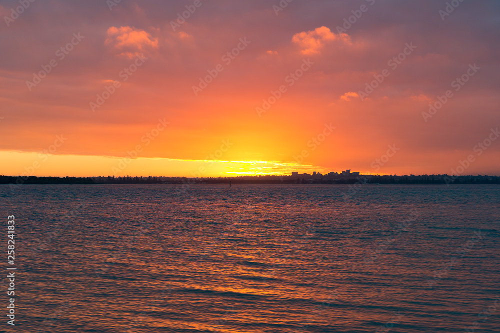 Naklejka premium Bright orange red sunset sky over water