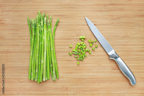 Fresh green asparagus and sliced on wooden board background with sharp knife.