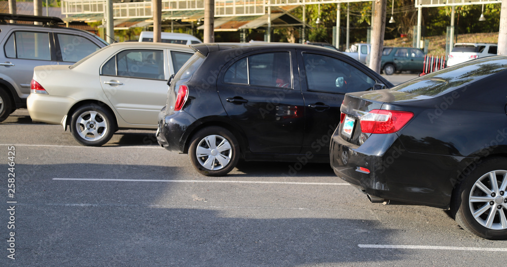 Closeup of back or rear side of black car and other cars parking in parking lot with natural background in bright sunny day. 