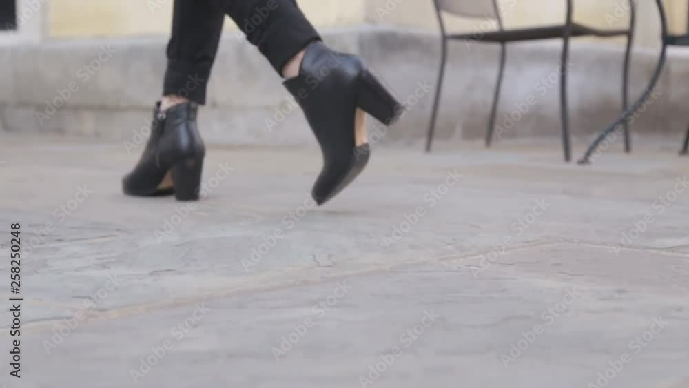 Medium follow shot of woman in fashionable boots walking away from a stone wall with a planter in the background. Medium follow shot of woman in fashionable boots walking away from a stone wall with a planter in the background.