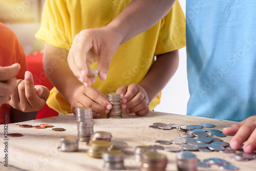 Hands of children are helping putting coins into piggy bank \ on white background
