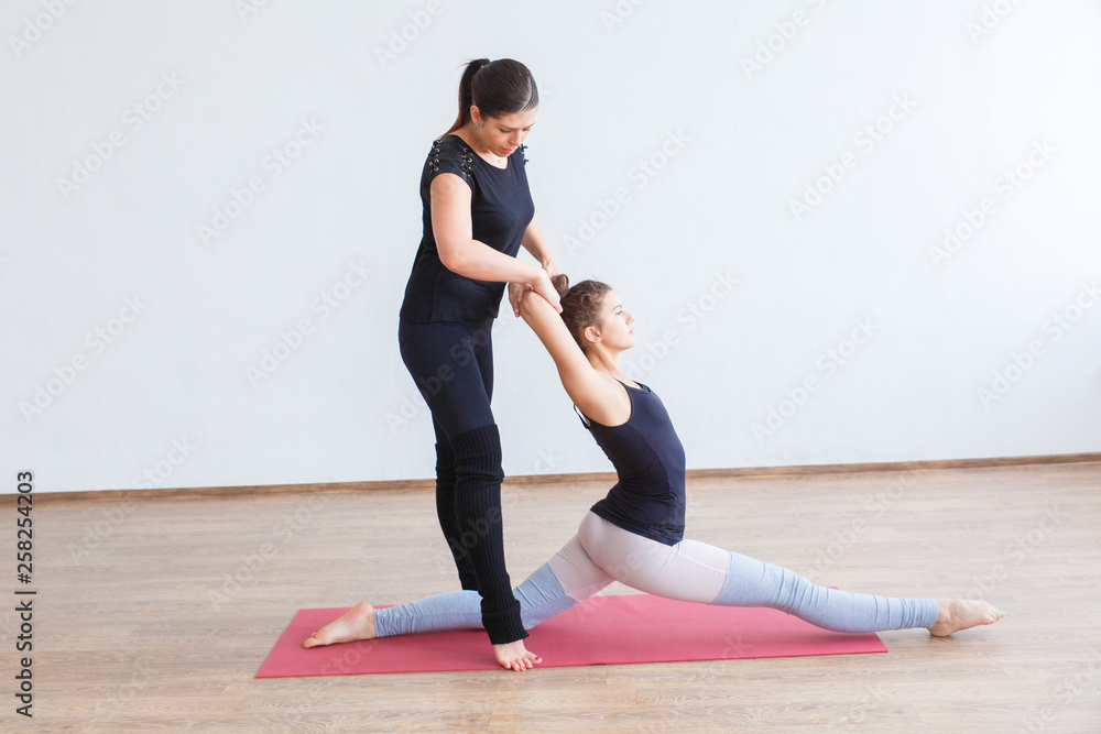 Two girls are engaged in stretching the body. The girl helps the other girl bend her back on the Mat. Two girls are engaged in stretching the body. The girl helps the other girl bend her back on the Mat.