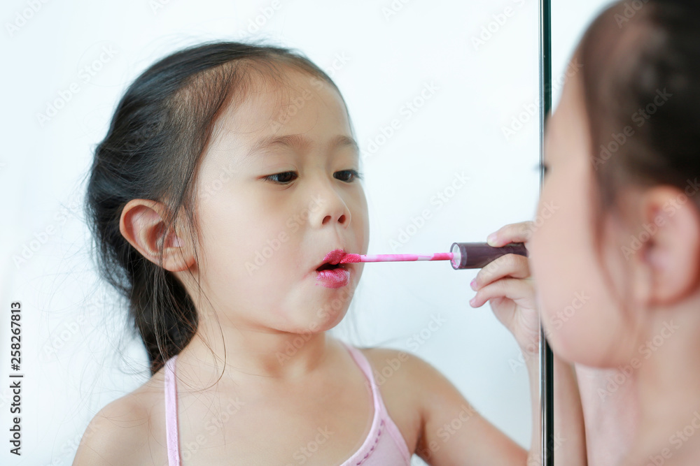 Cute little Asian child girl trying lip gloss near a mirror. Cute little Asian child girl trying lip gloss near a mirror.