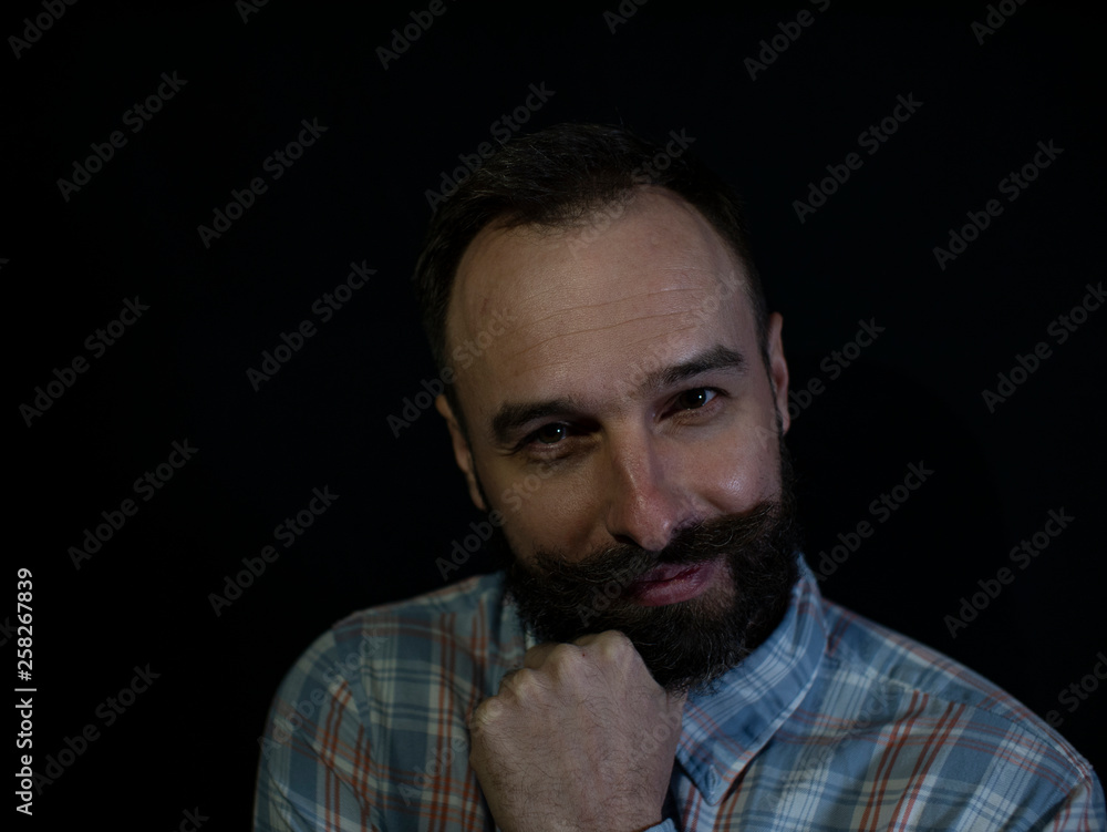 a man with a beard and mustache with a thoughtful sly face on a black background