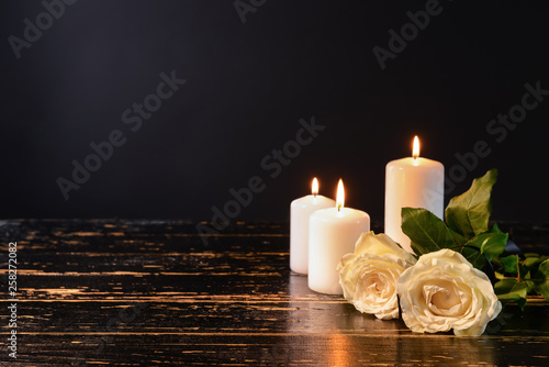 Valokuvatapetti Burning candles and flowers on table against black background