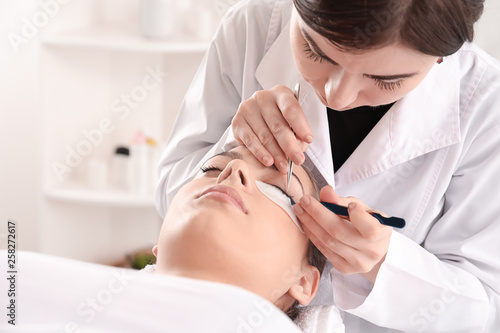 Young woman undergoing eyelash extension procedure in beauty salon