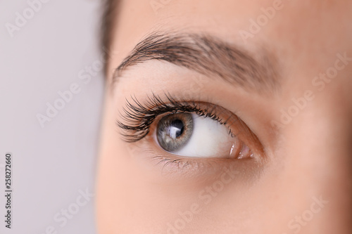 Beautiful young woman with eyelash extensions on light background, closeup