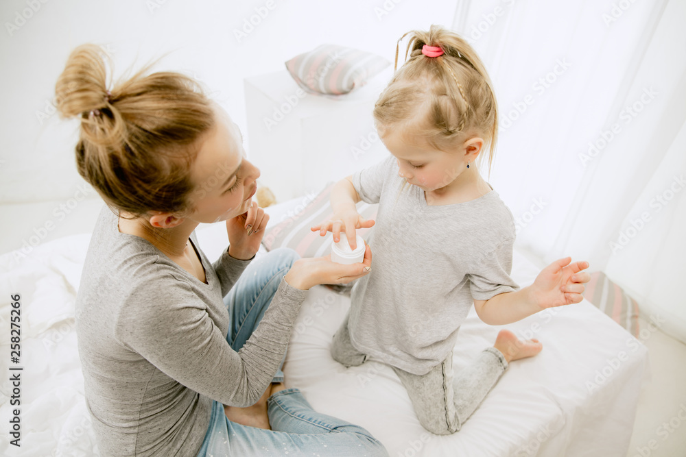 Young mother and her little daughter at home at sunny morning. Soft pastel colors. Happy family time on weekend. Mother's Day concept. Family, love, lifestyle, motherhood and tender moments concepts. Young mother and her little daughter at home at sunny morning. Soft pastel colors. Happy family time on weekend. Mother's Day concept. Family, love, lifestyle, motherhood and tender moments concepts.
