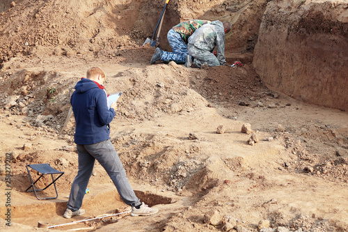 Archaeological excavations. The archaeologists in a digger process, researching the tomb with human bones, drawing the human remains. Real digger process. Outdoors, copy space.