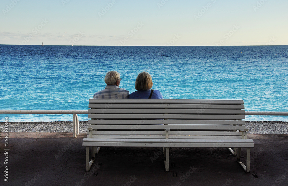 Old couple sitting on bench viewing the  blue Mediterranean. Promenade des Angles, Nice, France.