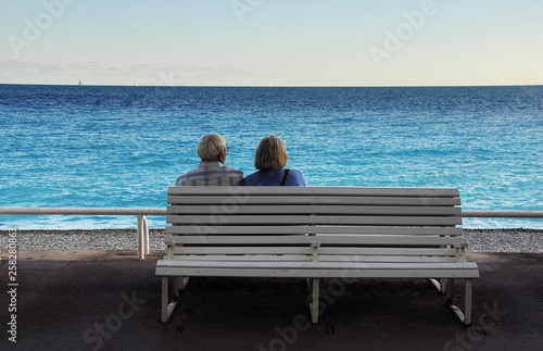 Old couple sitting on bench viewing the blue Mediterranean. Promenade des Angles, Nice, France.