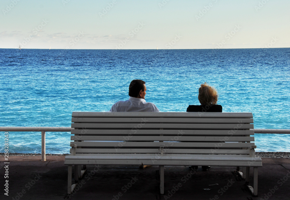 Couple sitting on a bench enjoying the view of azur blue Mediterranean. Promenade des Angles, Nice, France. Copy space