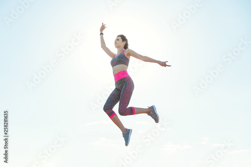 Fototapeta Naklejka Na Ścianę i Meble -  Sporty young girl in the morning on pier in jump, practicing yoga. Woman do gymnastics outdoors. Health and Yoga Concept. Female lifestyle meditation for fitness lifestyle the nature background
