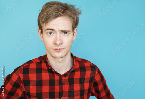 young serious male teenager in red shirt on blue background