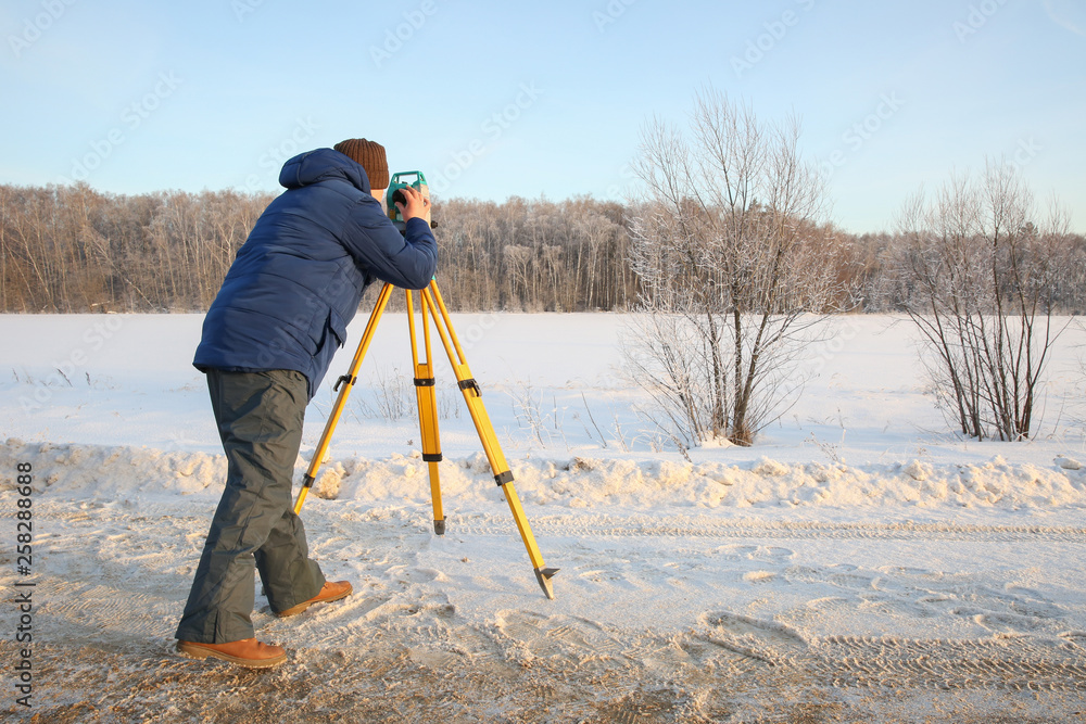the surveyor takes measurements. the surveyor works in the winter on the nature. a man works with a total station.