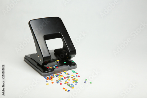 black office hole punch with confetti isolated on white background.  Hole puncher sprinkled whith colorful confetti.  photo