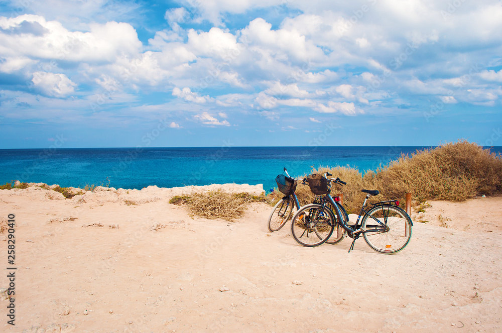 Fototapeta premium Two bicycles with baskets parked against deep blue azure water
