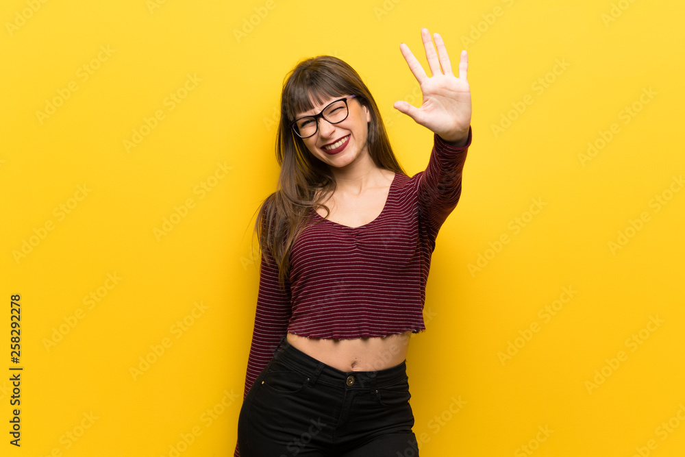 Woman with glasses over yellow wall counting five with fingers Woman with glasses over yellow wall counting five with fingers