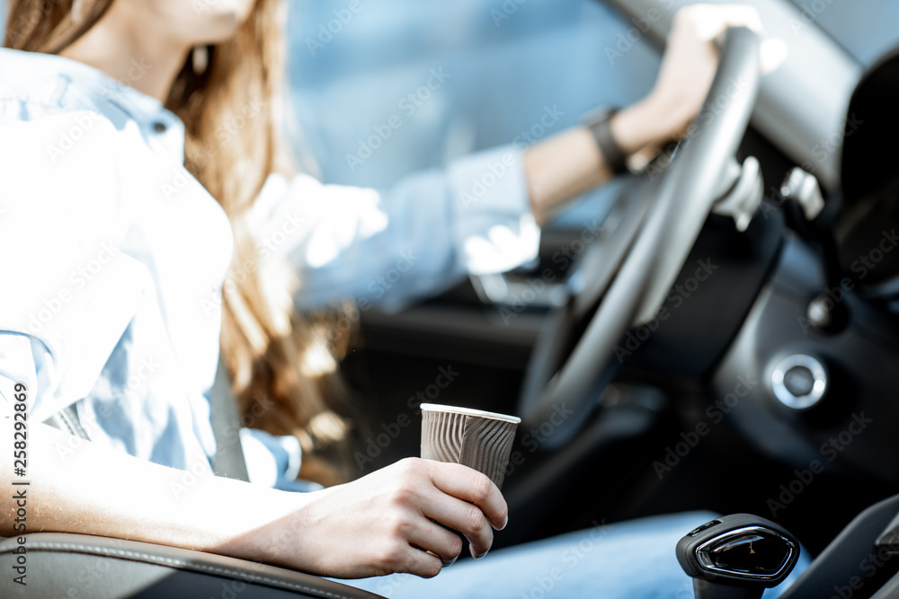 Woman holding coffee cup while driving a car, close-up view focused on the cup Woman holding coffee cup while driving a car, close-up view focused on the cup