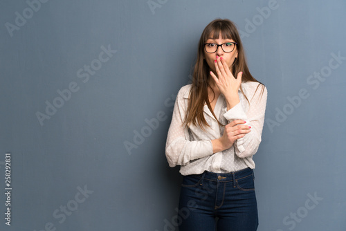 Woman with glasses over blue wall covering mouth with hands for saying something inappropriate