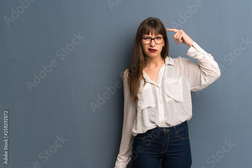 Woman with glasses over blue wall making the gesture of madness putting finger on the head