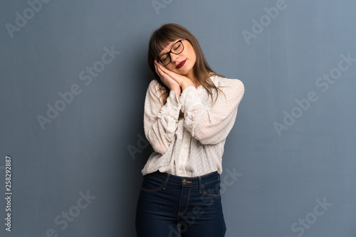 Woman with glasses over blue wall making sleep gesture in dorable expression © luismolinero