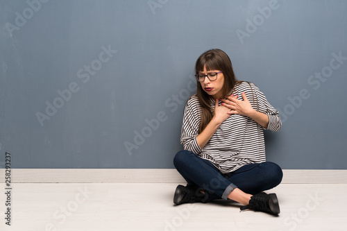 Woman with glasses sitting on the floor having a pain in the heart