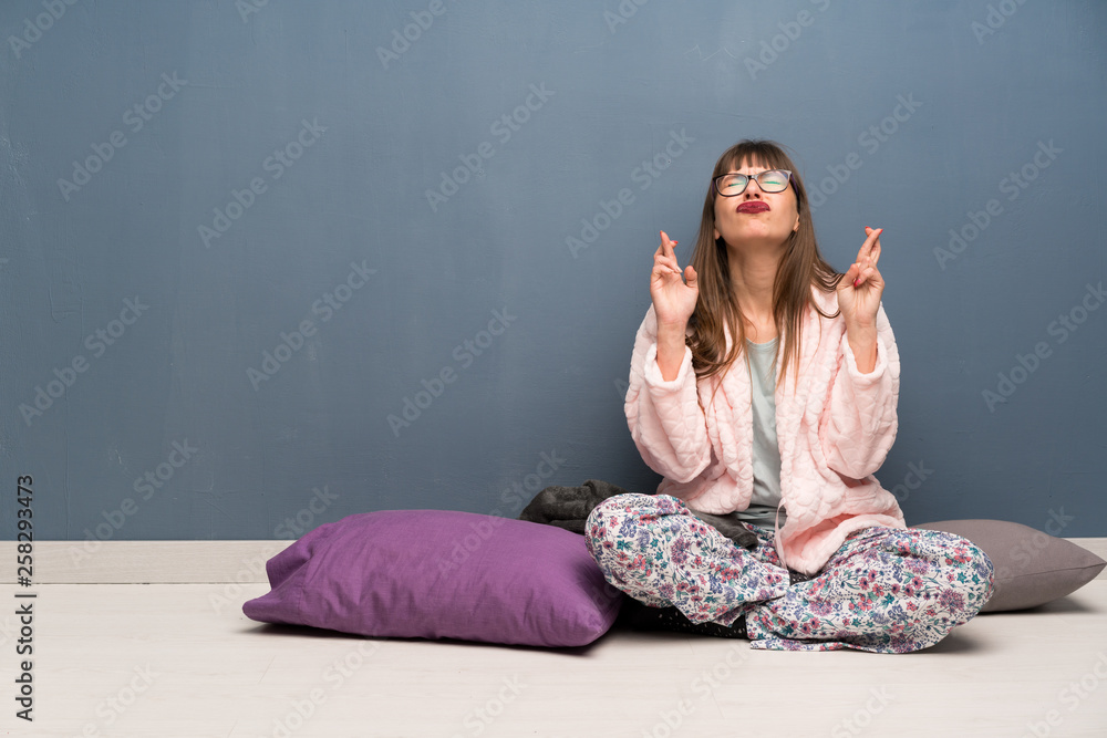 Woman in pajamas on the floor with fingers crossing and wishing the best Woman in pajamas on the floor with fingers crossing and wishing the best
