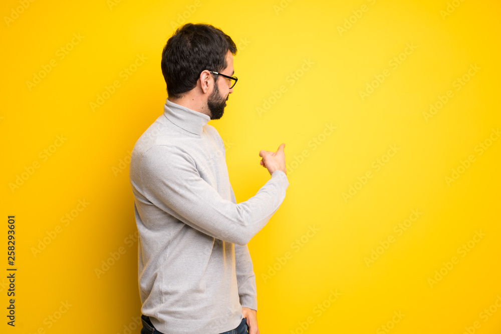 Man with beard and turtleneck pointing back with the index finger Man with beard and turtleneck pointing back with the index finger