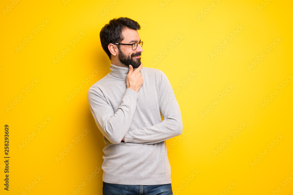 Man with beard and turtleneck looking to the side with the hand on the chin