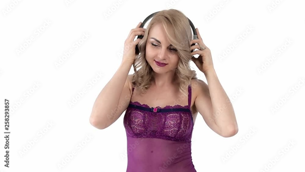Portrait of Young attractive blonde woman dressed in burgundy lingerie listen to romantic music at black wireless headphones and dancing. Slow motion, isolated on white background. Portrait of Young attractive blonde woman dressed in burgundy lingerie listen to romantic music at black wireless headphones and dancing. Slow motion, isolated on white background.