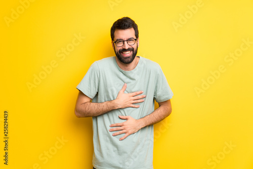 Man with beard and green shirt smiling a lot while putting hands on chest