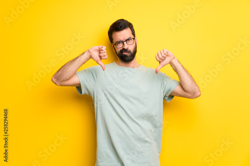 Man with beard and green shirt showing thumb down with both hands photo