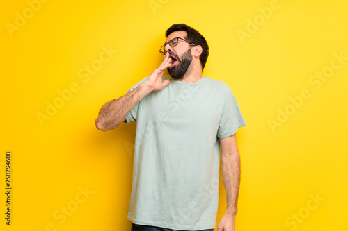 Man with beard and green shirt yawning and covering wide open mouth with hand © luismolinero