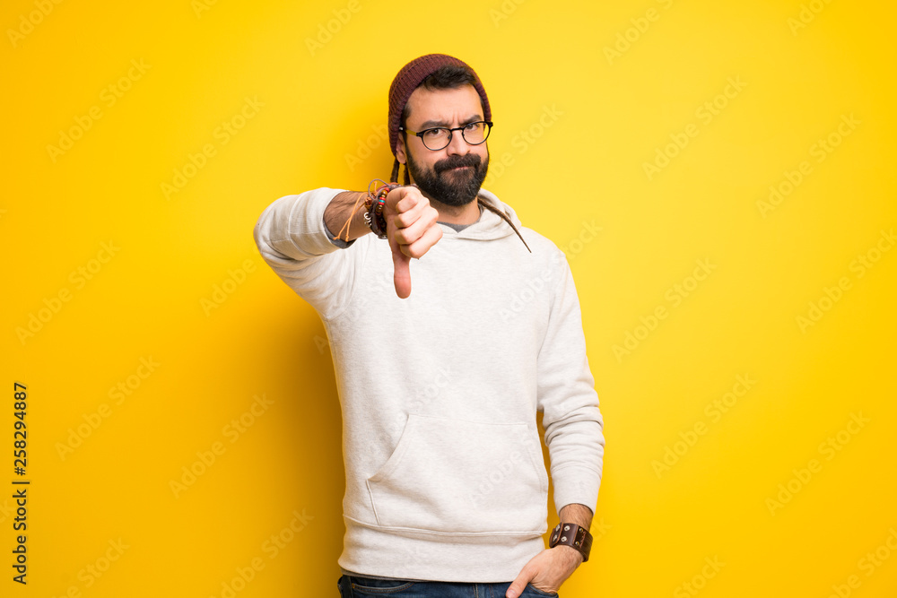Hippie man with dreadlocks showing thumb down sign with negative expression Hippie man with dreadlocks showing thumb down sign with negative expression