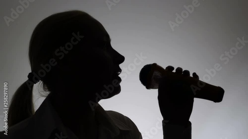 Silhouette of a woman on a white background. A woman sings emotionally into a microphone.