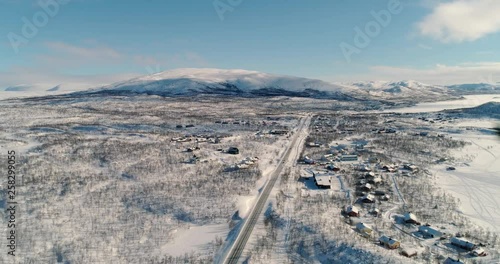 Kilpisjarvi village, C4k aerial, tilt, drone shot, towards a north scandinavian town, in snowy arctic circle wilderness, on a sunny, winter day, in Kilpisjrvi, Enontekio, Lapland, Finland photo