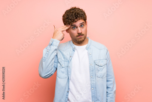 Blonde man over pink wall with problems making suicide gesture