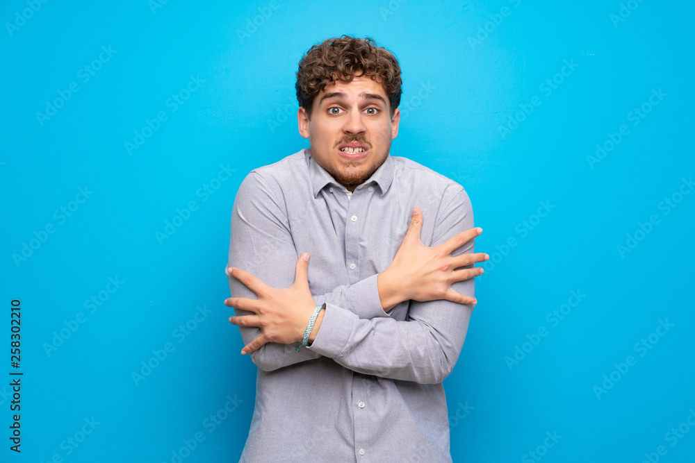 Blonde man over blue wall freezing Blonde man over blue wall freezing