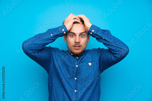 Tableau sur toile Blonde man over isolated blue wall with surprise facial expression