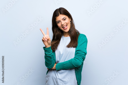 Teenager girl over blue wall smiling and showing victory sign